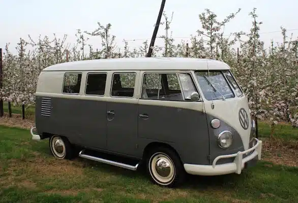 Een betoverend beeld van een vintage Volkswagen-busje versierd als trouwauto, omringd door een weelderige boomgaard vol kleurrijke bloesems