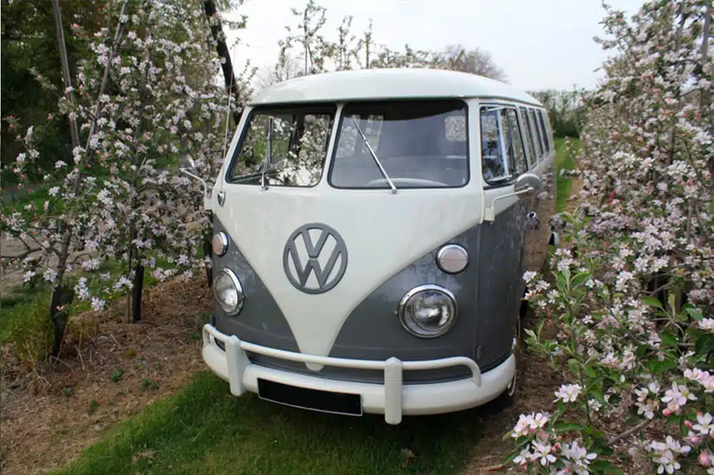 Een rustieke trouwauto in de vorm van een prachtig gerestaureerd Volkswagen-busje, geparkeerd tussen de boomgaard vol fruitbomen in volle bloei