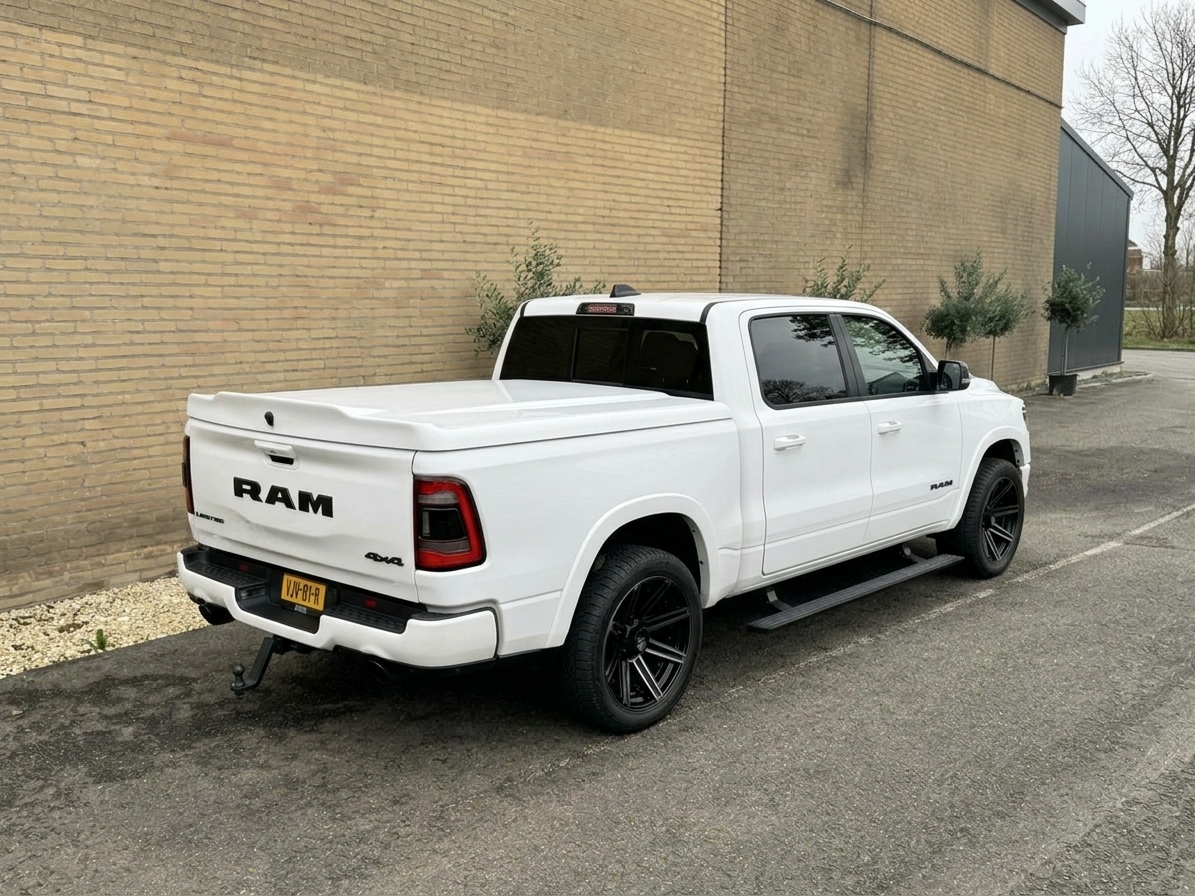 Witte Dodge RAM pick-up met afgedekte laadbak en treeplanken, schuin van achteren gezien
